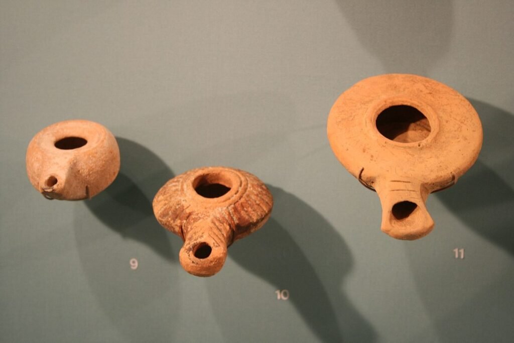 Three small reddish clay oil lamps on a museum wall