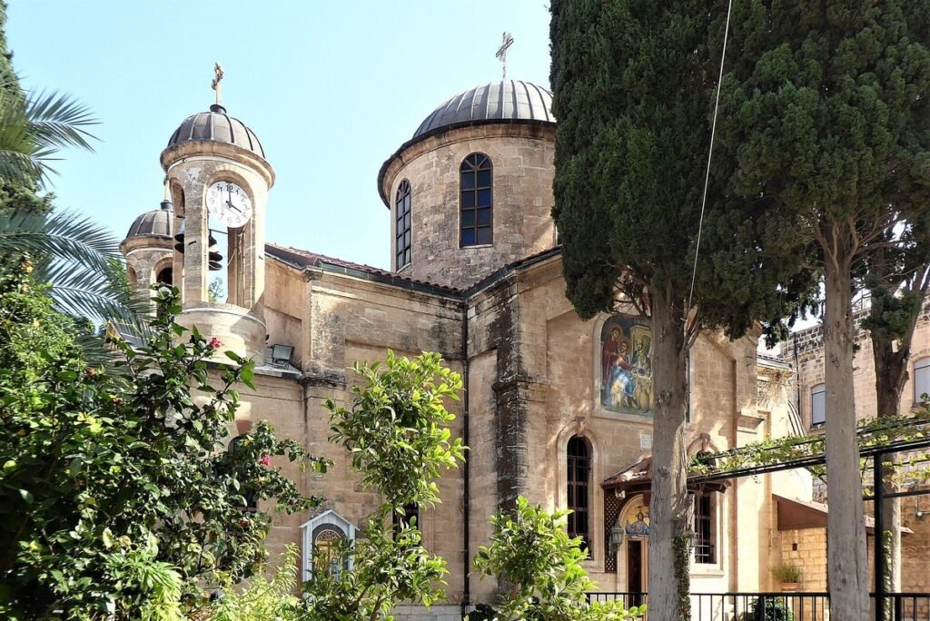 Church with domes and a bell tower among cypresses in Kafr Kanna