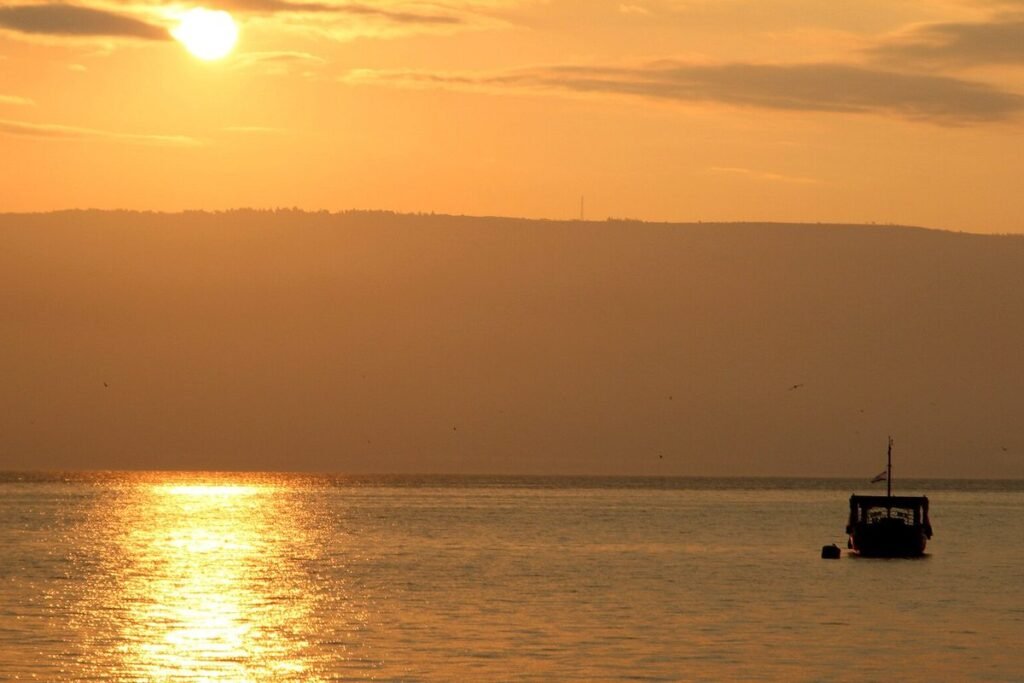 The sun rises over the hills by the Sea of Galilee, a boat on the water